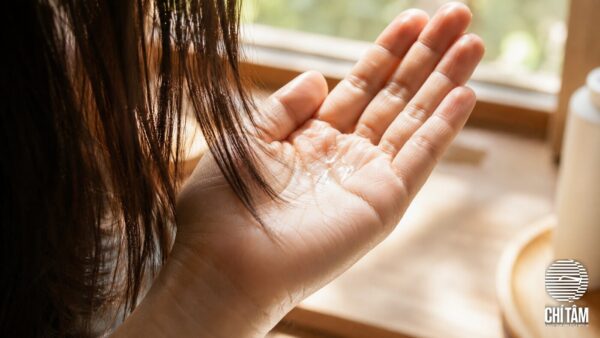 Vài giọt serum dưỡng tóc trong suốt trên lòng bàn tay bên cạnh lọn tóc nâu tự nhiên
