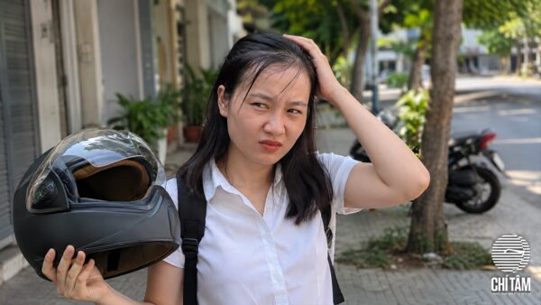 Cô gái tháo mũ bảo hiểm, tóc xẹp bẹt vùng đỉnh đầu trên vỉa hè Sài Gòn